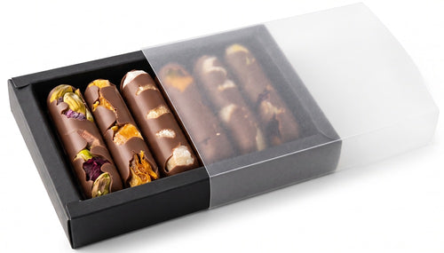 An open black gift box with a clear sleeve, holding a row of chocolate fingers topped with pistachios and dried fruit.